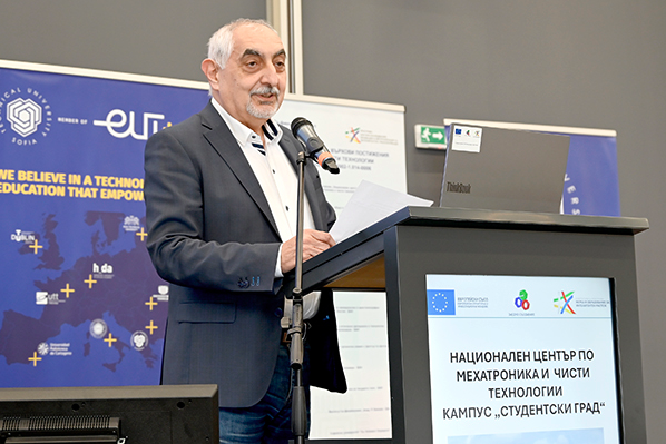 Мъж с побеляла коса чете от листове на трибуна с надпис „Национален център по мехатроника“.